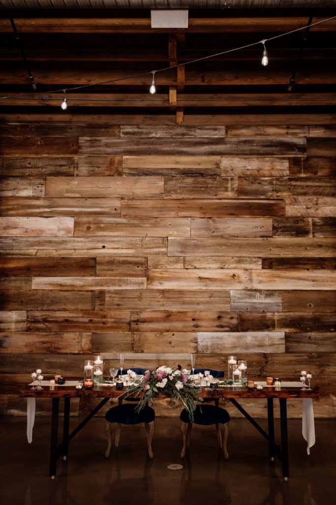 The head table at The Bridge Lemont with a wooden wall and gorgeous flowers