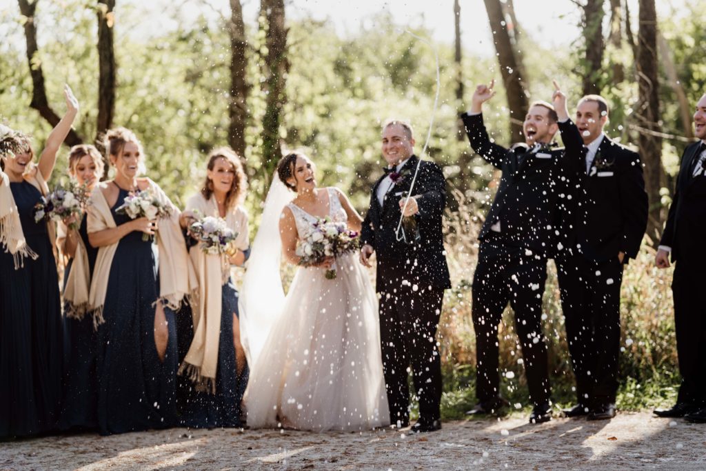 Bridal party laughs and cheers as the groom pops champagne and sprays them during bridal party photos in Chicago