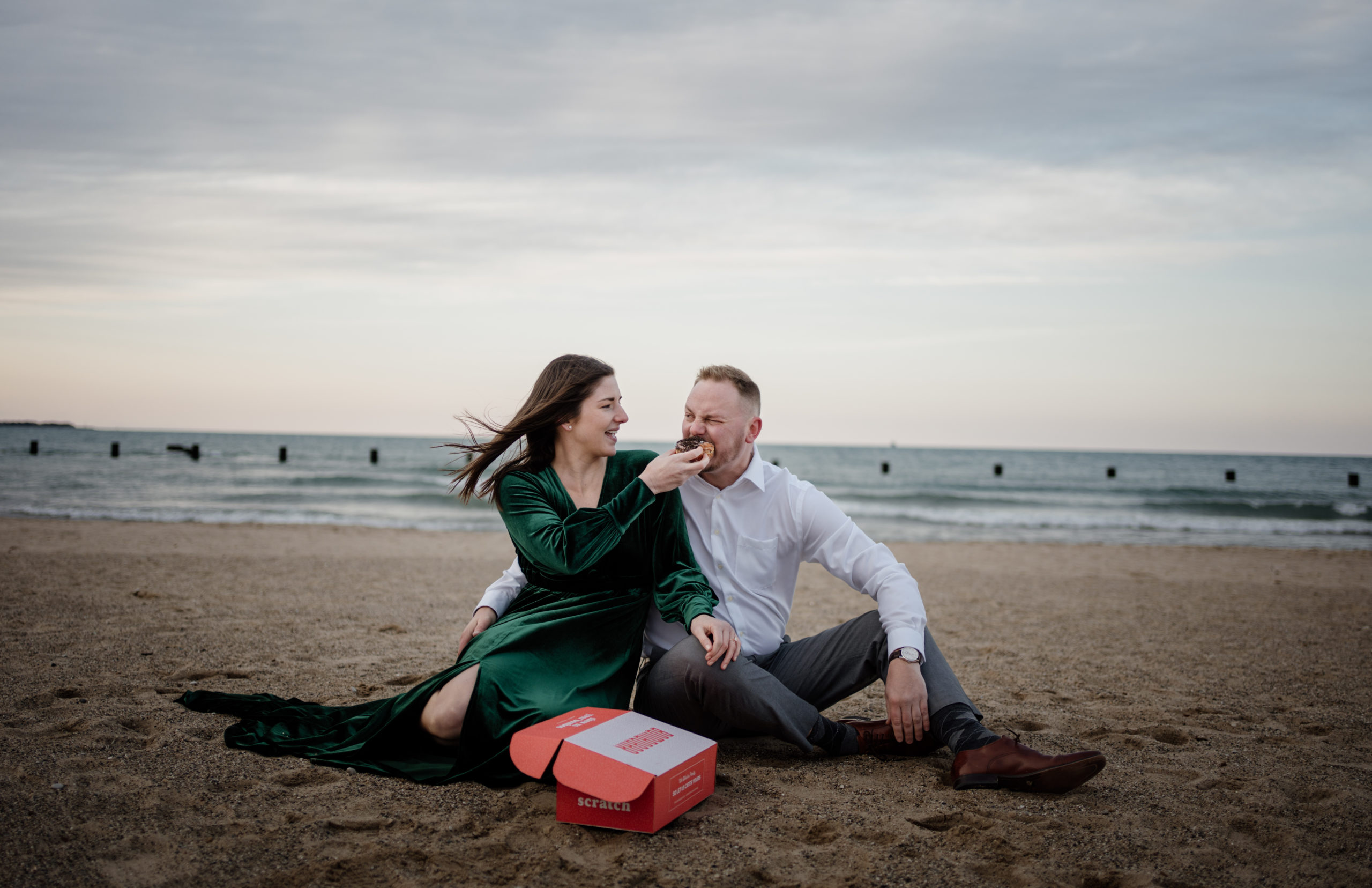 couple eating donuts at North Ave Beach for engagement photos